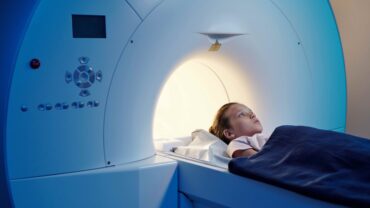 little-patient-under-blue-towel-lying-on-long-table-of-mri-scan-machine